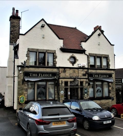 The Fleece Traditional Pub Exterior Cars Exterior view of The Fleece, a traditional two-story building with a white and black facade, featuring large windows with signage, flanked by parked cars.