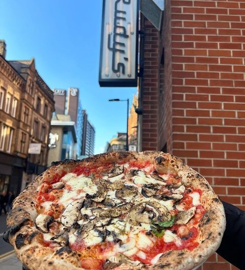 Rudys Pizza Napoletana Chapel Allerton Fresh Mushroom Pizza Outdoor Hand holding a freshly baked mushroom pizza in front of Rudy’s Pizza Napoletana – Chapel Allerton, with the restaurant's sign visible in the background.