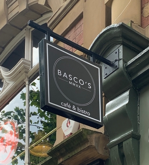 Charming Bistro Signage in Urban Setting Black and white sign for BASCO'S café & bistro hangs from a green awning, surrounded by historic brick architecture.