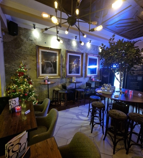 Cozy Festive Ambiance with Art Decor Cozy dining area with wooden tables, green chairs, festive Christmas tree, and warm lighting creating a welcoming atmosphere.