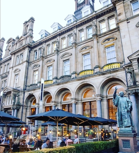 Elegant Outdoor Dining with Historic Architecture Elegant outdoor dining area with umbrellas, historic building facade, and a statue, creating a vibrant atmosphere.