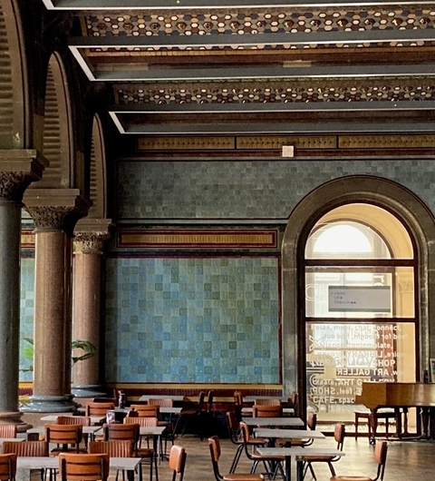 Elegant Tiled Walls and Cozy Seating Elegant café interior with tall columns, blue tiled walls, and wooden tables arranged for dining.
