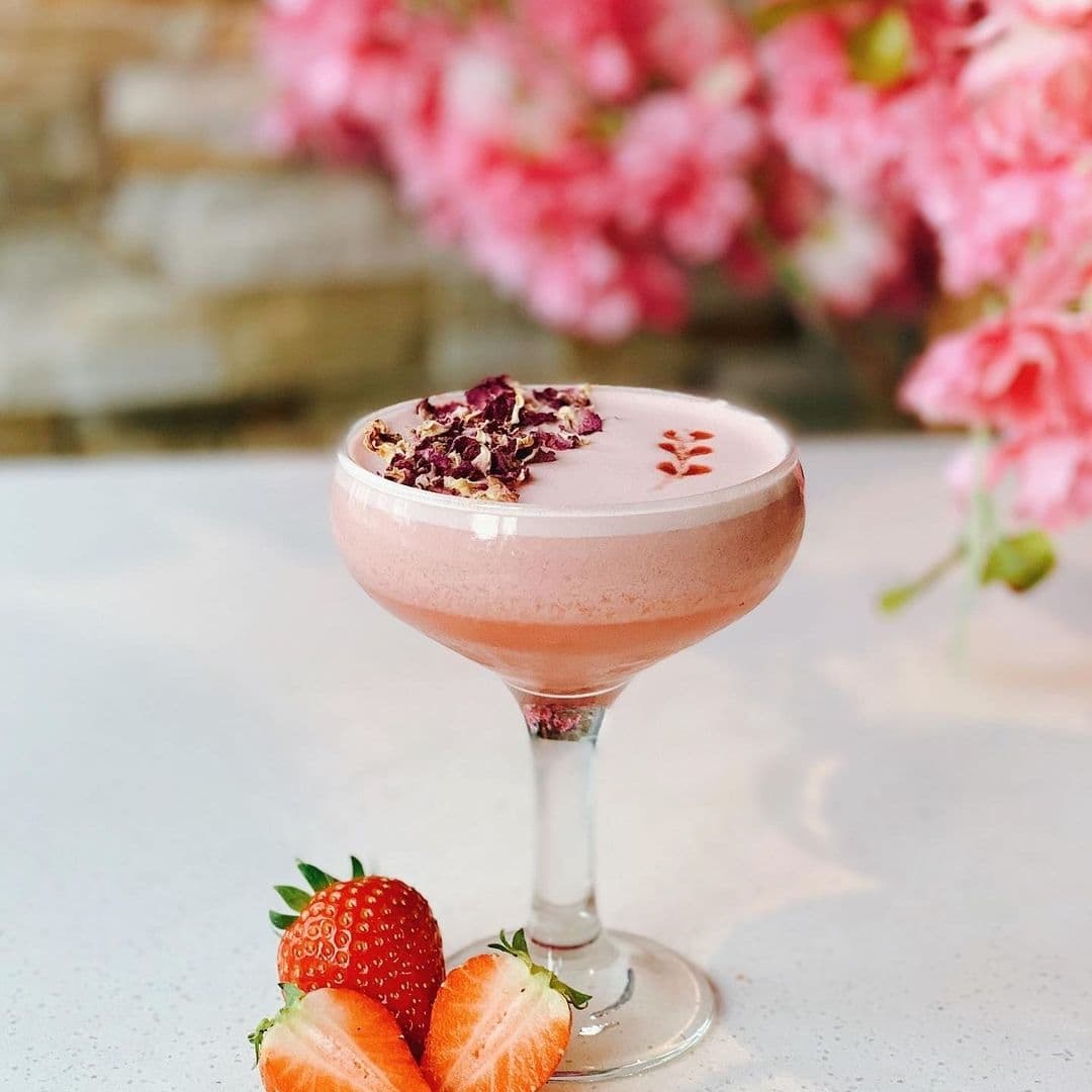 Blue Sakura Pink Cocktail Floral Garnish Strawberries Elegant pink cocktail garnished with dried flowers, presented in a stemmed glass with fresh strawberries on the side, at Blue Sakura.