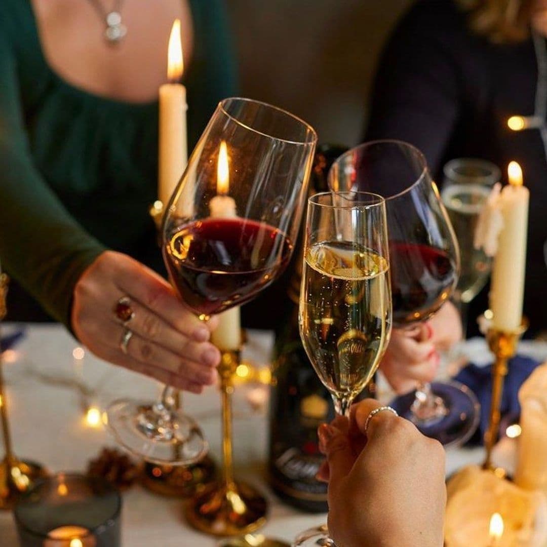 BrasserieBlanc_ElegantWineToast_CandlelightCelebration Elegant dining experience at Brasserie Blanc with close-up of hands toasting with glasses of red wine and champagne, surrounded by warm candlelight ambiance.
