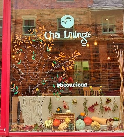 Cha Lounge Autumn Display Window Decor "Autumn-themed window display at Cha Lounge featuring the shop's name, decorative leaves, and an assortment of pumpkins and gourds, with the hashtag #becurious."