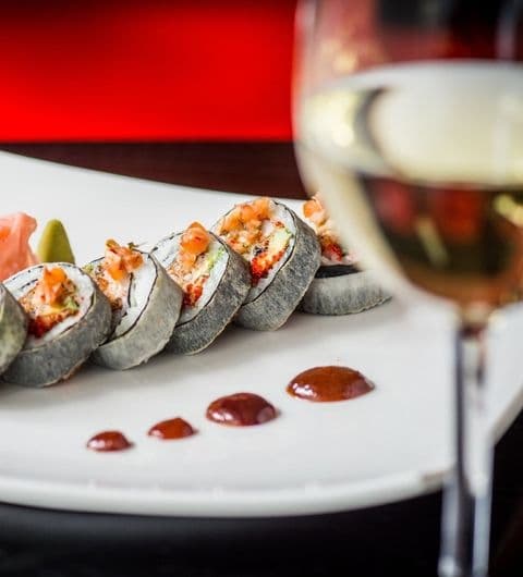 Chino Latino_Sushi Platter_White Wine_Elegant Dining Sushi rolls with toppings on a white plate, Chino Latino, with a glass of white wine in the background.