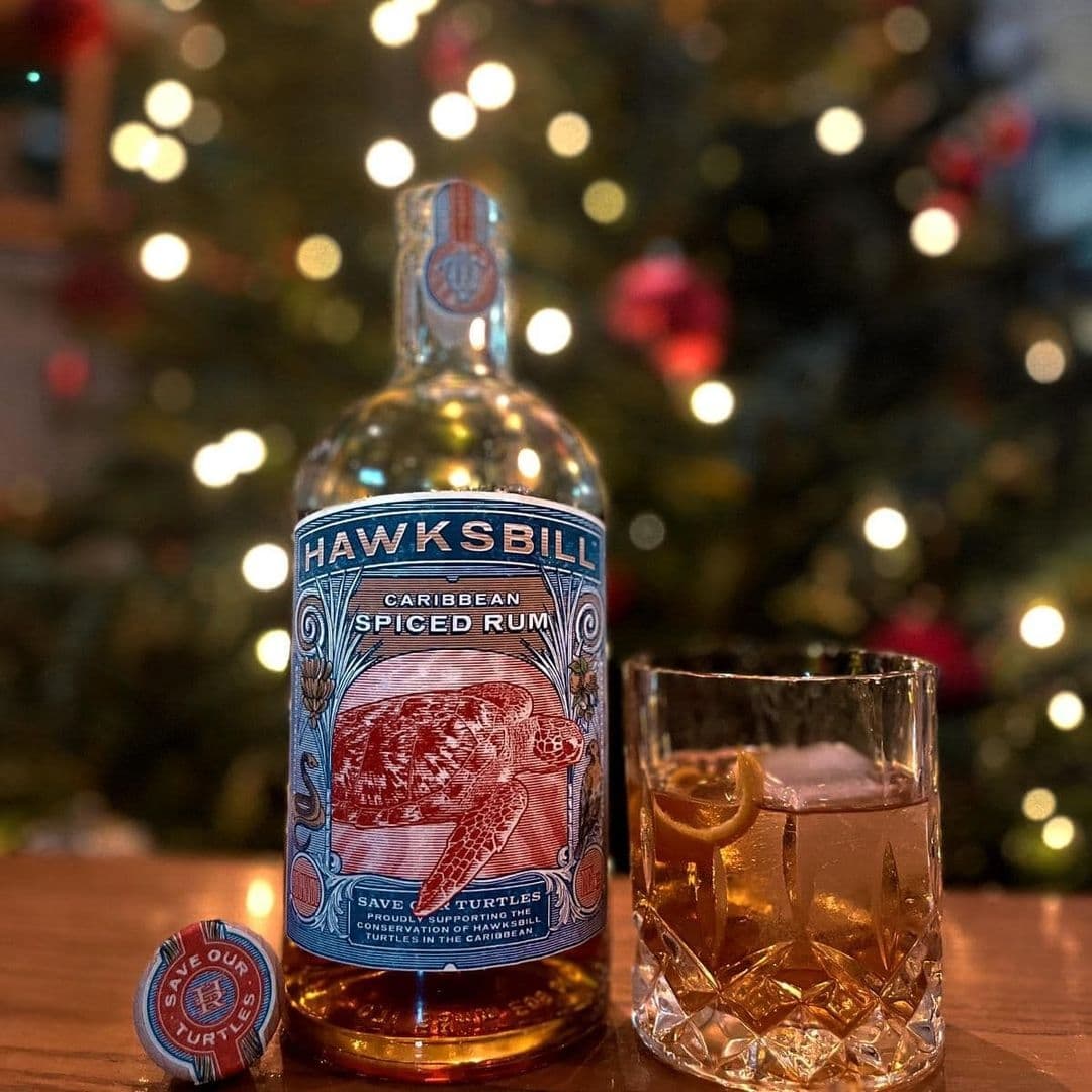 Coopers Bar and Brasserie Caribbean Spiced Rum Festive Decor Bottle of Hawksbill Caribbean Spiced Rum with a filled glass on a table at Coopers Bar and Brasserie, festive lights blurred in the background.
