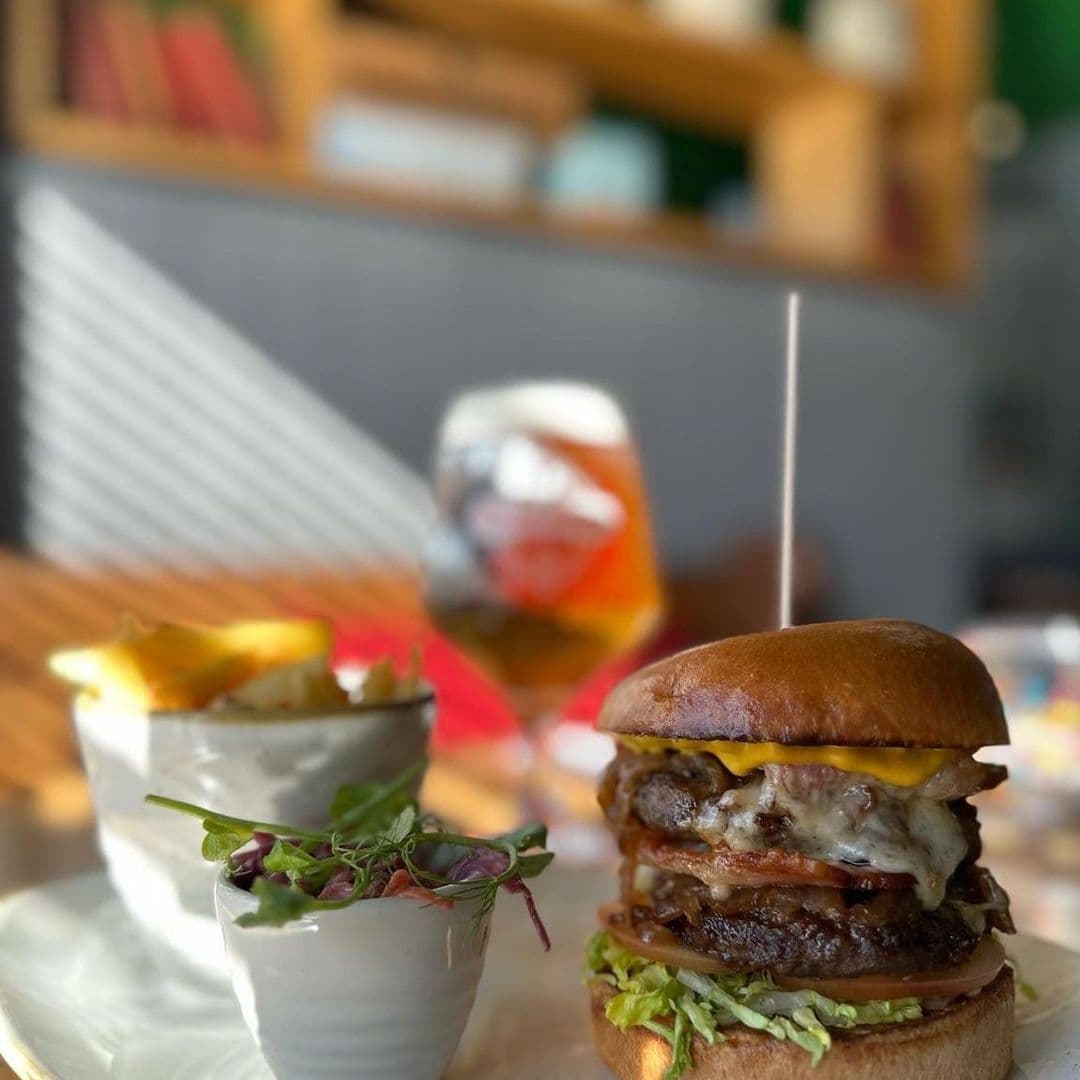 Coopers Bar and Brasserie Gourmet Burger Beer Dining Gourmet burger with melted cheese and fresh garnishes served on a plate with a side of fries at Coopers Bar and Brasserie, with a pint of beer in the background.