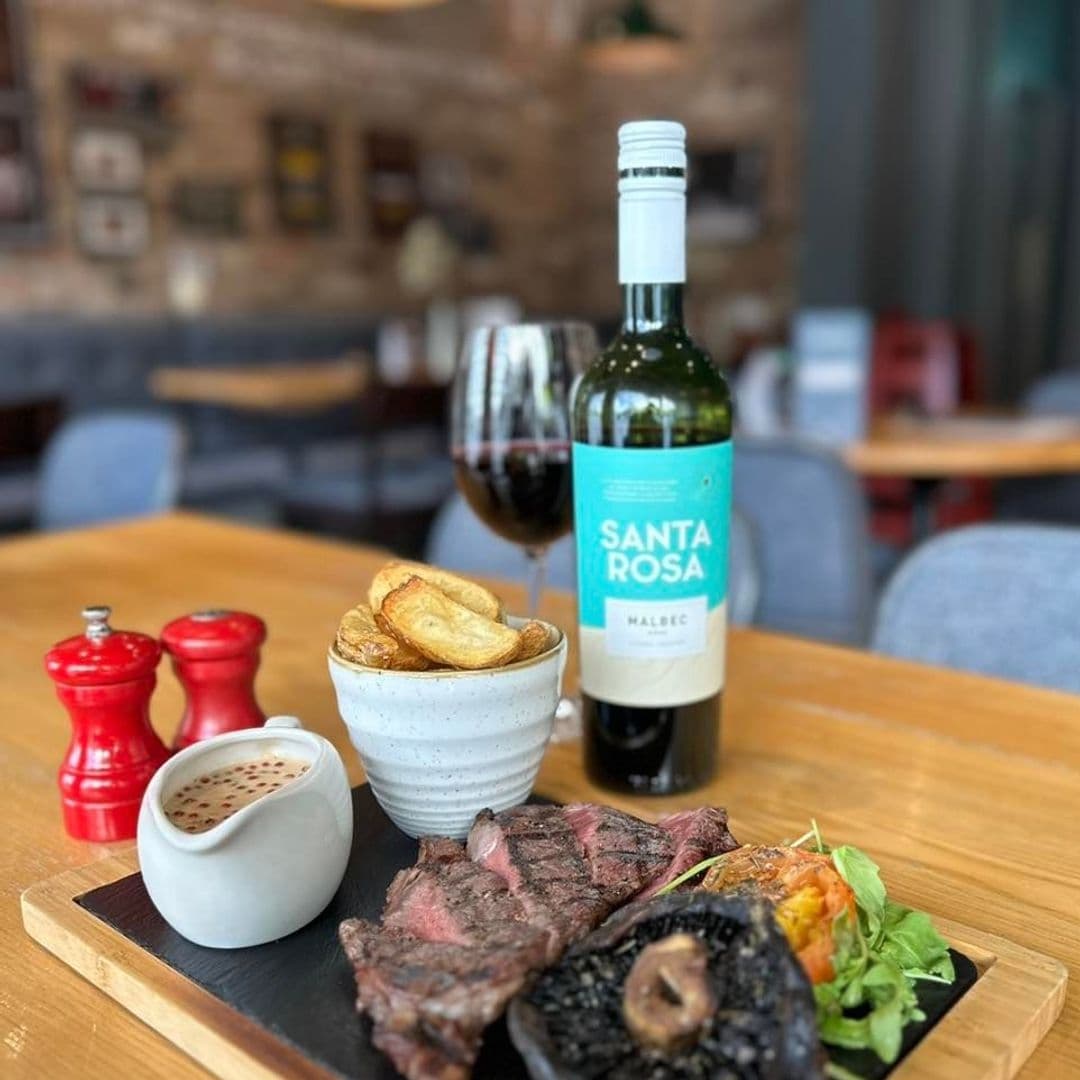 Coopers_Bar_and_Brasserie_Steak_Wine_Dining_Experience Grilled steak and roasted potatoes served on a wooden board with a side of peppercorn sauce, accompanied by a glass and bottle of Santa Rosa Malbec wine, with salt and pepper shakers in the foreground, at Coopers Bar and Brasserie.