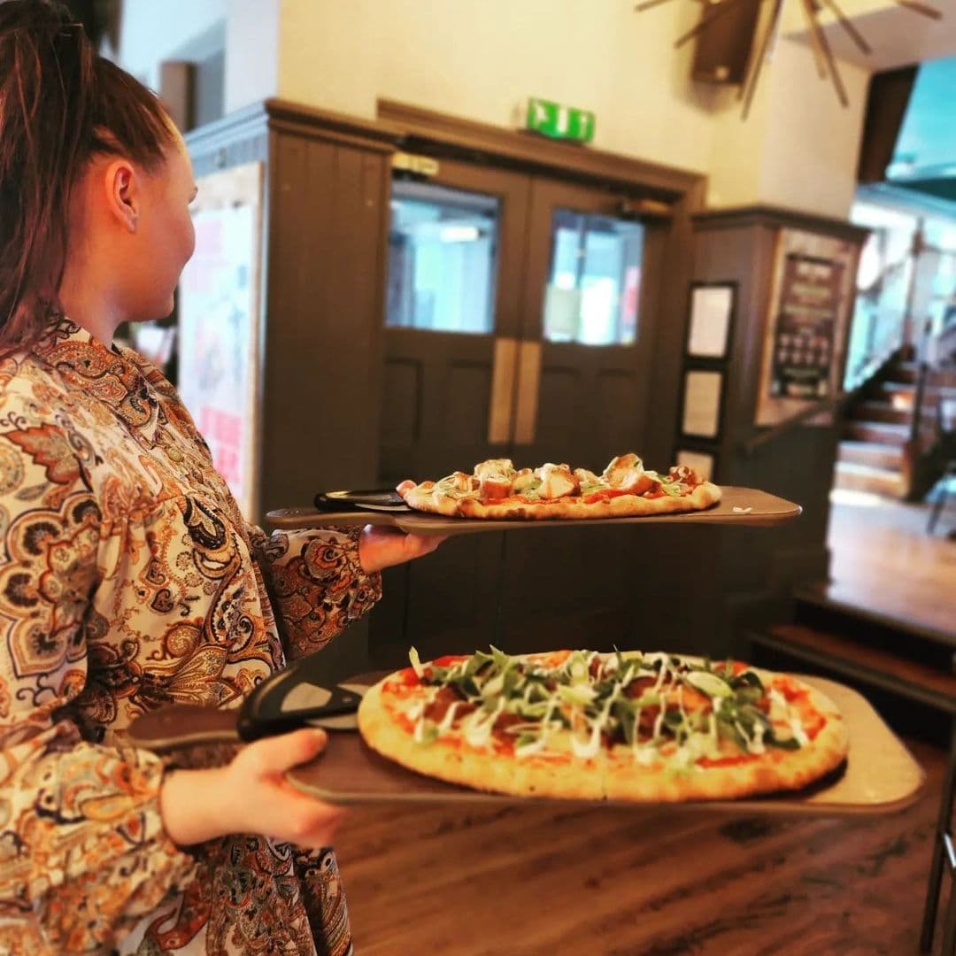 Editors Draught Waitress Serving Pizza Restaurant Interior Waitress serving freshly made pizza at Editor's Draught, with a cozy restaurant interior in the background.