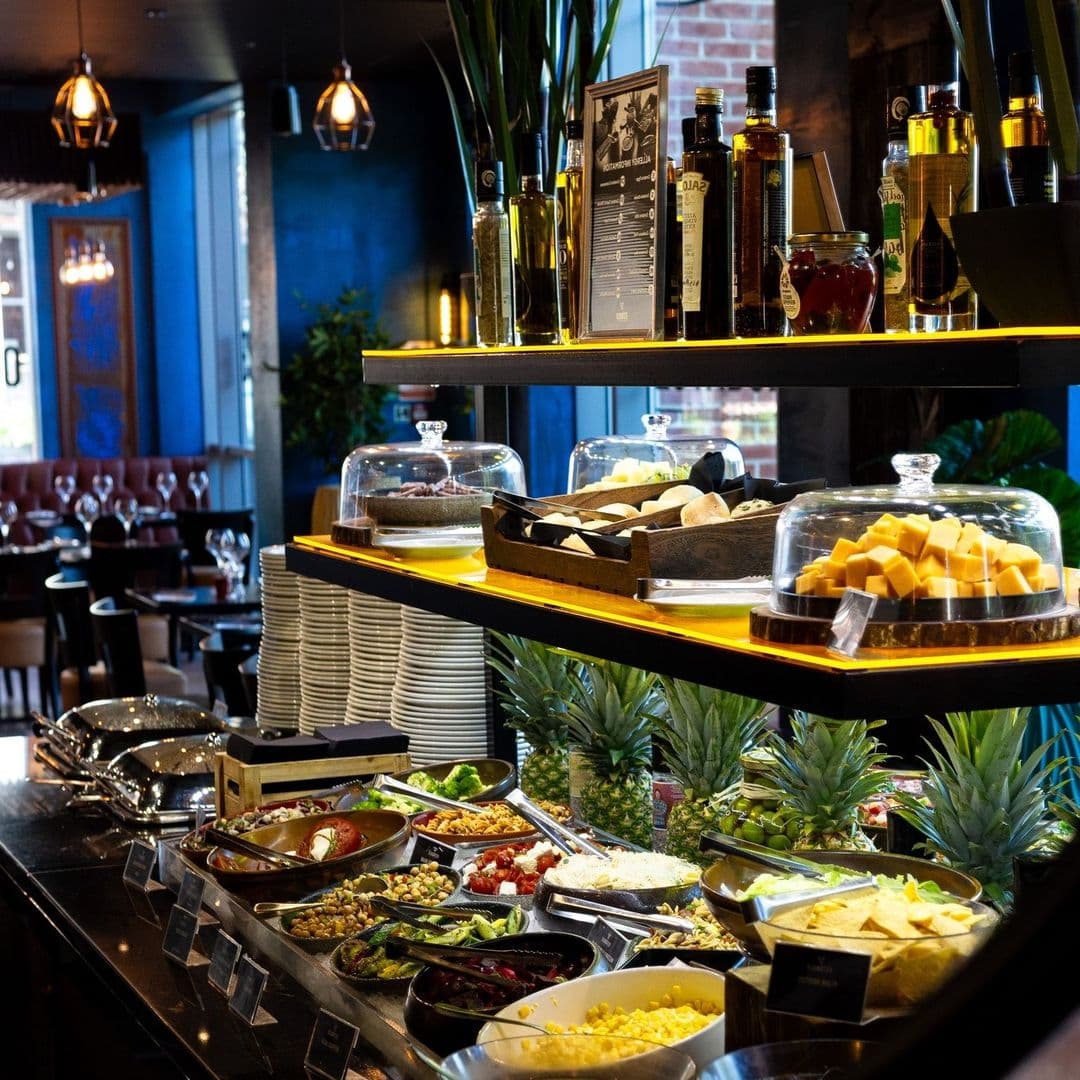 Estabulo The Light Cosy Ambience Buffet Spread Modern Interior Interior view of Estabulo – The Light, featuring a well-lit buffet with a variety of dishes, fresh fruits, and cheeses, complemented by a stylish bar area in the background.