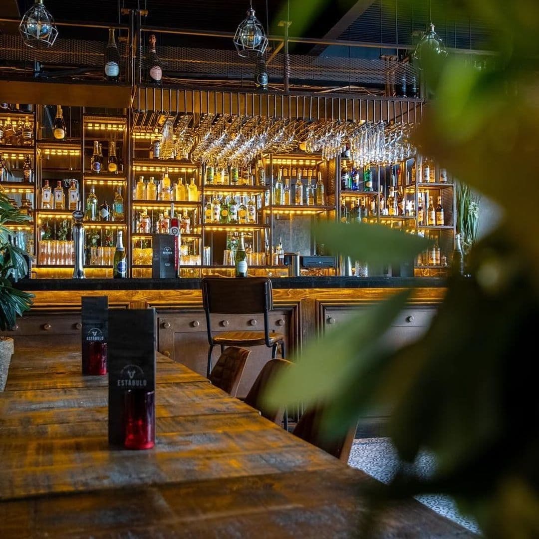 Estabulo The Light elegant bar interior wooden furnishings Interior of Estabulo – The Light, showcasing a warmly lit bar area with an extensive selection of bottles on backlit shelves, elegant hanging glassware, and wooden furnishings.