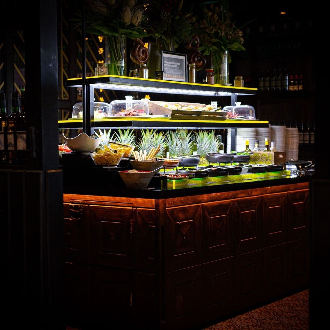Estabulo The Light_Gourmet Buffet Selection_Ambient Lighting Elegant buffet setup at Estabulo – The Light, featuring a selection of fresh foods, condiments, and plates, warmly illuminated and inviting.