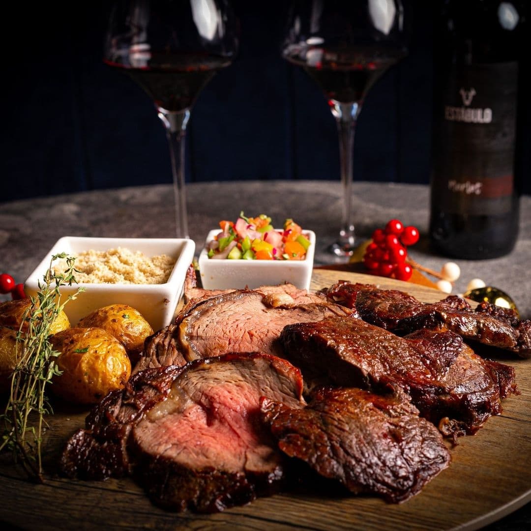 Estabulo The Light_Gourmet Steak Dinner Wine Pairing Succulent slices of roasted beef served with golden roasted potatoes, fresh salad, and creamy sauce on a wooden board, accompanied by red wine at Estabulo – The Light.
