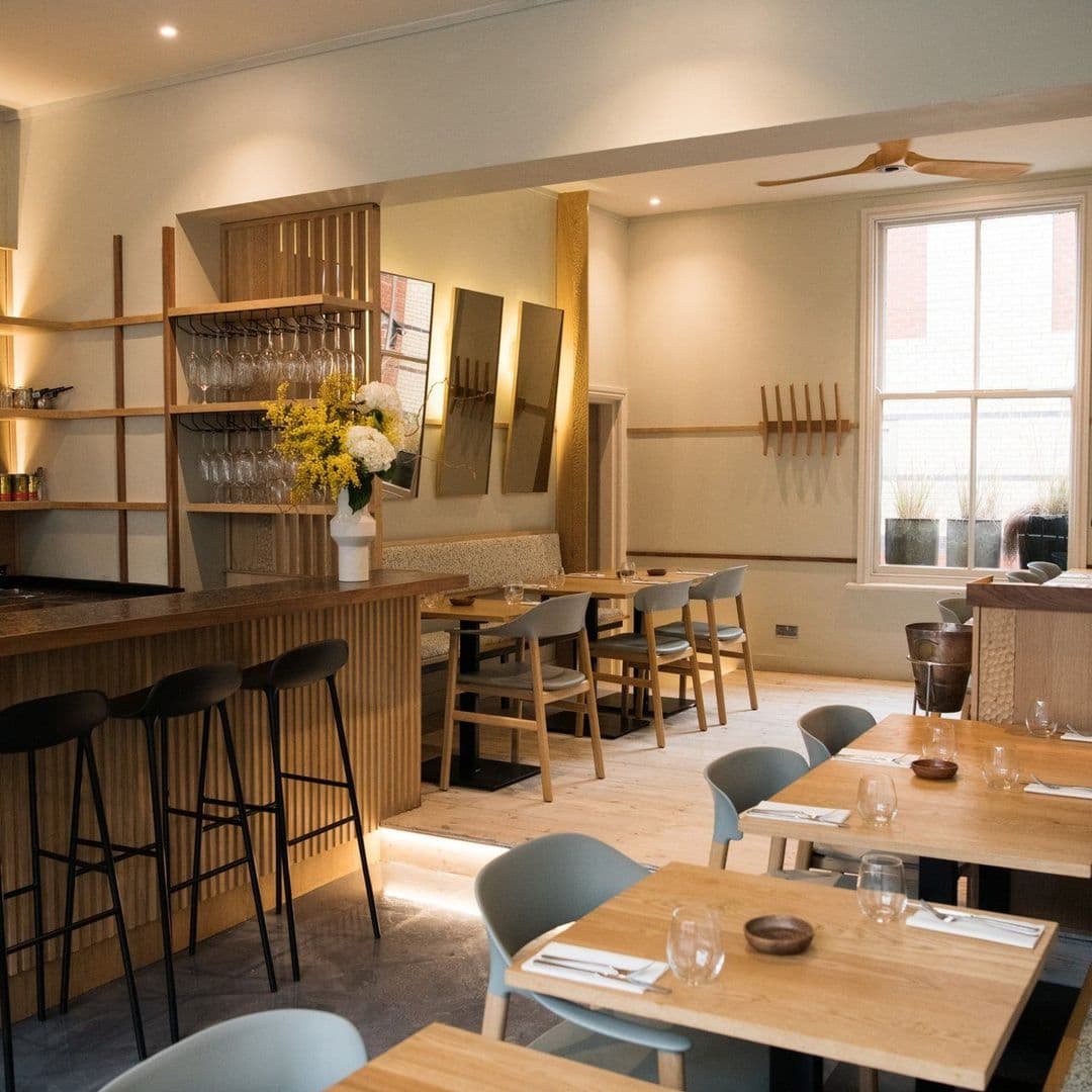 FINT_modern_dining_interior_wooden_furniture_cozy_decor Interior of FINT restaurant featuring modern wooden furniture, elegant shelving with glassware, and decorative mirrors on the wall.