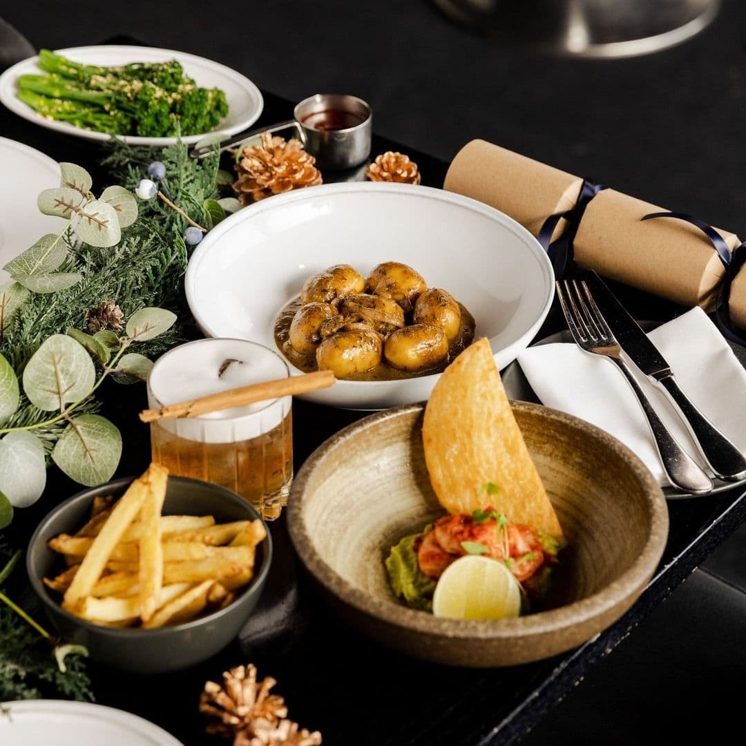 Gaucho Delicious Traditional Cuisine Elegant Setting Assorted gourmet dishes at Gaucho, featuring roasted baby potatoes, golden French fries, and a bowl of shrimp with a slice of lemon, accompanied by cutlery wrapped in a napkin and decorative greenery.