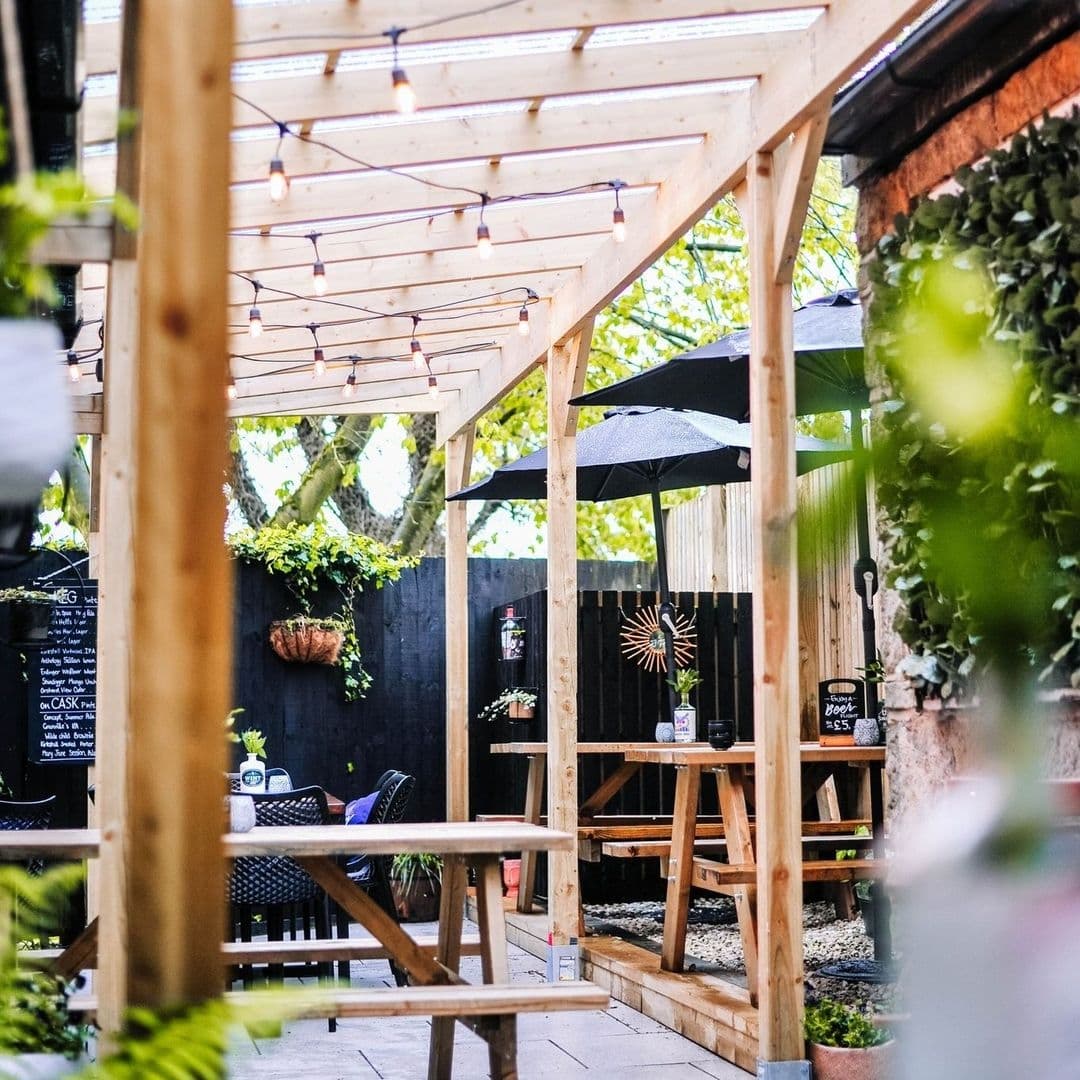 Granvilles Beer Gin House outdoor patio lights ambiance Cozy outdoor seating area at Granvilles Beer & Gin House with wooden tables, string lights, and greenery.