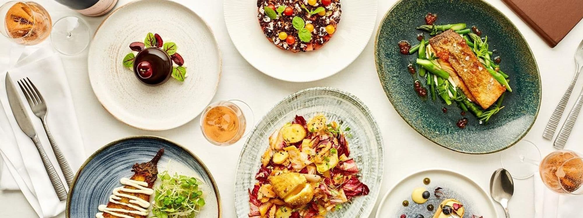 Elegant dining setup at H A R V E Y • N I C H O L S • Fourth Floor • Brasserie & Bar featuring a variety of gourmet dishes and glasses of rosé wine on a white linen-covered table.