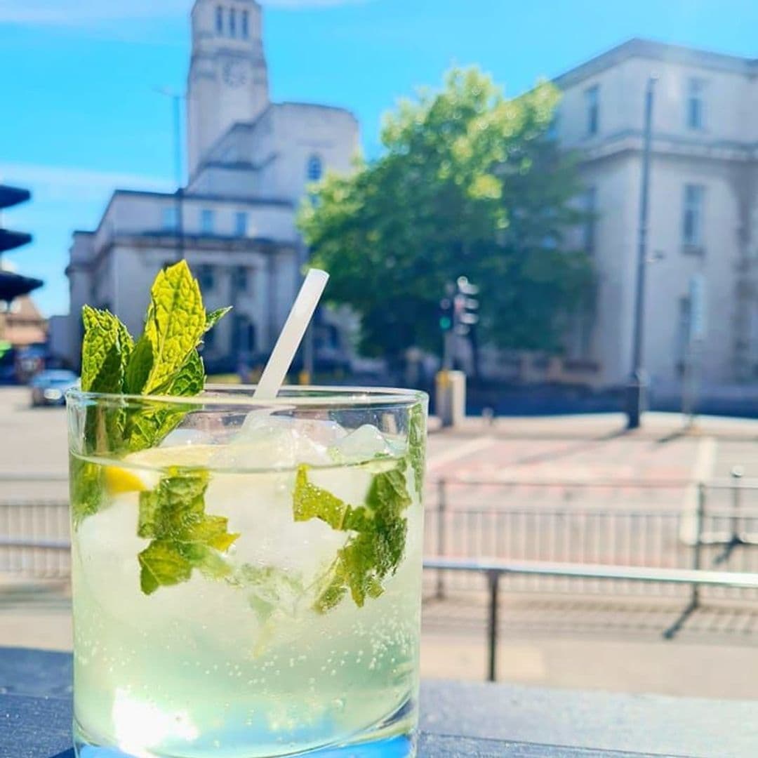 Handsome Bar Summer Cocktail Outdoor View Refreshing mojito cocktail at Handsome Bar with ice and mint leaves in a clear glass, overlooking a sunny street scene with historic architecture in the background.