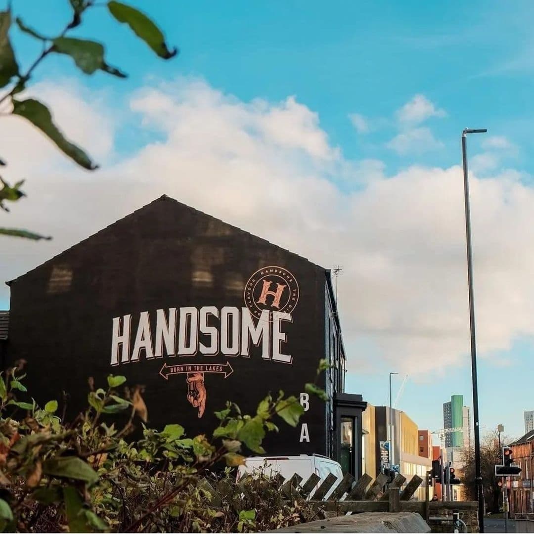 Handsome Bar Urban Exterior Blue Sky Exterior view of Handsome Bar with large sign on building facade, set against a blue sky with clouds, surrounded by urban scenery.