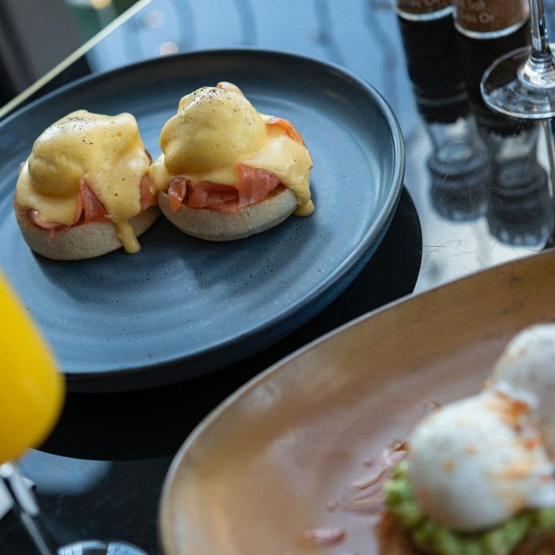 Harvey Nichols Fourth Floor Brasserie Bar Eggs Benedict Dish Eggs Benedict served on a blue plate at Harvey Nichols Fourth Floor Brasserie & Bar, with a glimpse of another breakfast dish and condiments in the background.