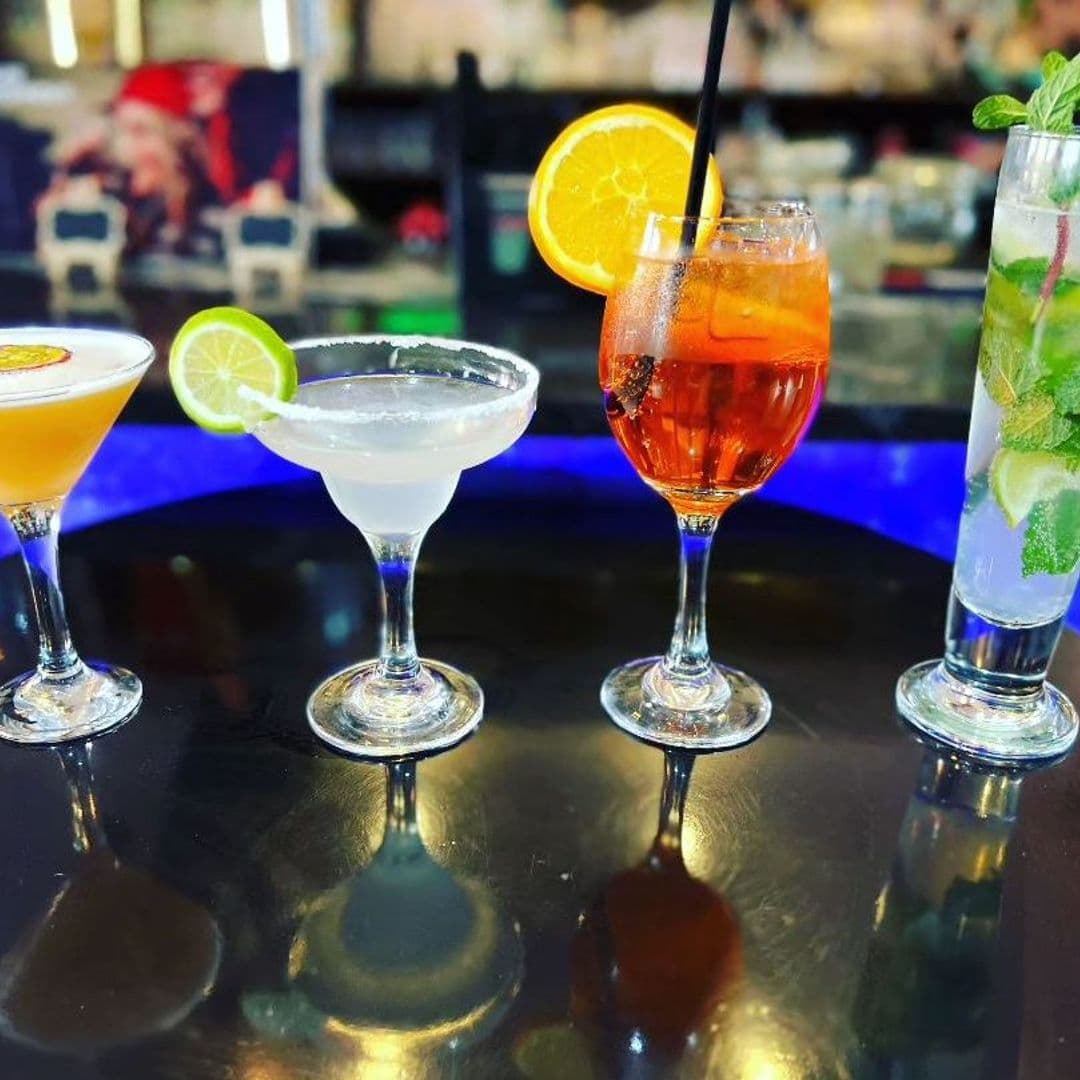 Indian Pakwaan_Cocktails Selection_Colorful Drinks_Garnished Glasses Assorted cocktails on a bar counter at Indian Pakwaan, featuring a margarita, an orange garnished drink, an Aperol spritz, and a mojito with fresh mint.