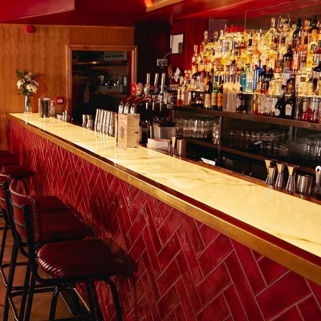 Jakes Bar Still Room Red Tiled Counter Warm Ambiance Interior of Jake's Bar & Still Room showcasing the polished bar counter with red tiles, lined with stools and a well-stocked bar with various bottles of liquor.