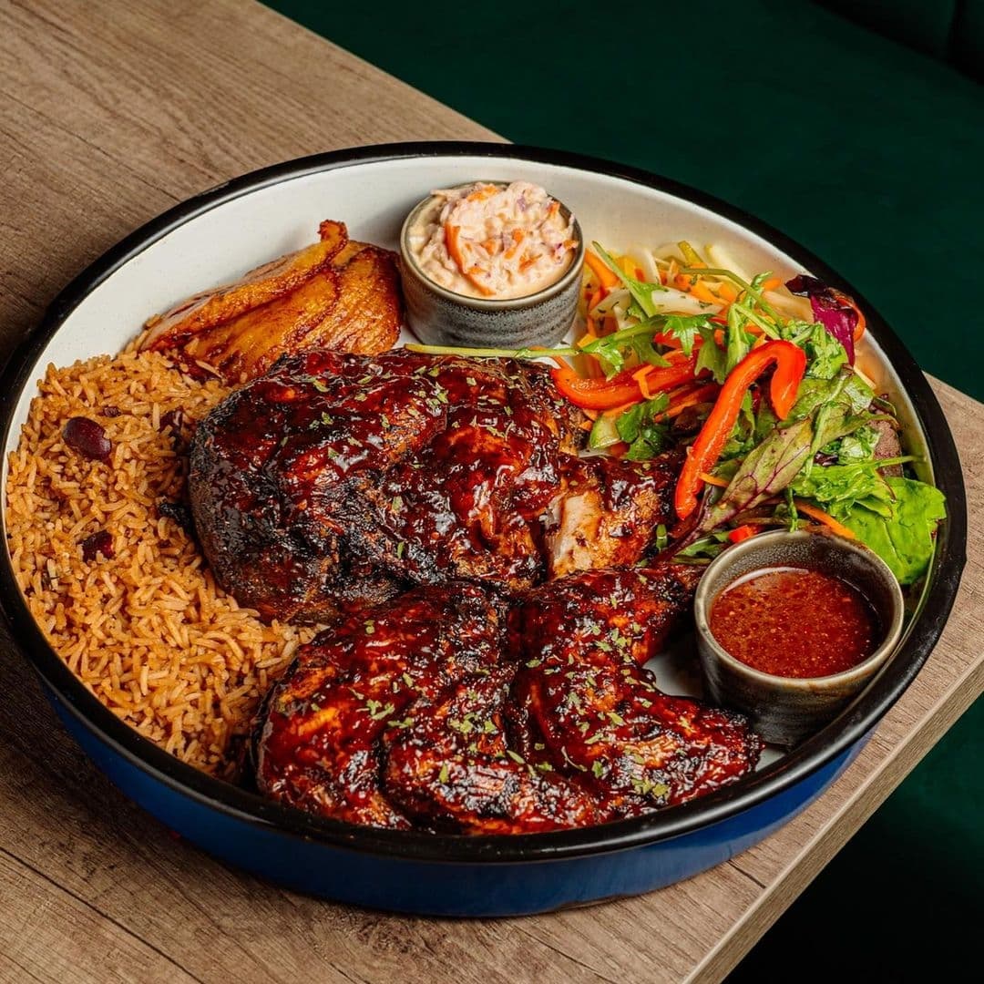 Jamrock Delicious Jerk Chicken Platter Local Cuisine Alt text: "Delicious traditional meal at Jamrock featuring jerk chicken, rice and peas, fried plantains, coleslaw, mixed salad, and dipping sauce."
