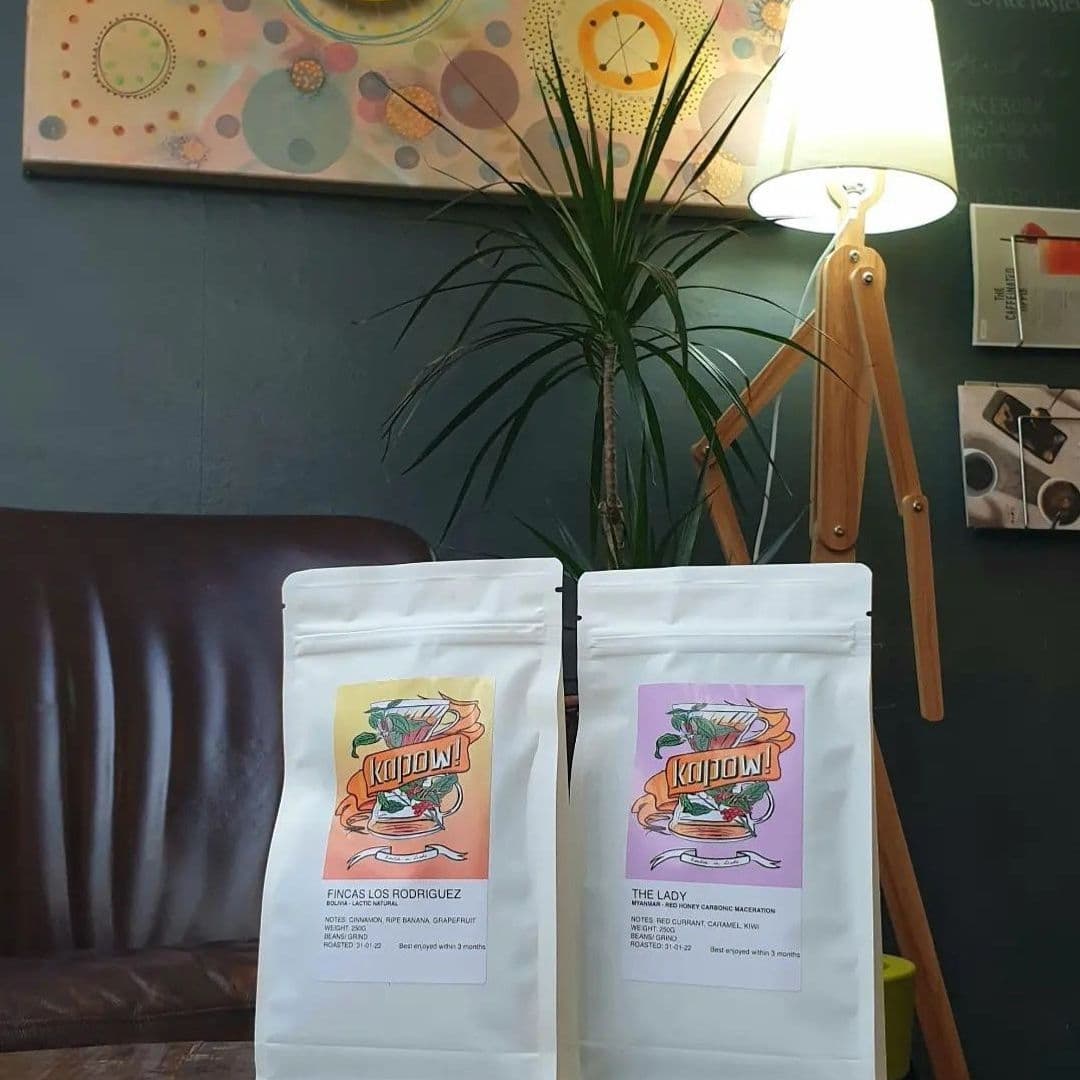 Kapow Coffee Thorntons Arcade Coffee Bags Interior Decor Two bags of Kapow Coffee on a table at Kapow Coffee – Thorntons Arcade, with a decorative plant and lamp in the background.