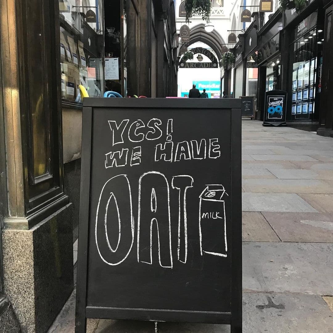 Kapow Coffee Thorntons Arcade Oat Milk Sign Arcade View Sidewalk sign outside Kapow Coffee – Thorntons Arcade with the message "YES! WE HAVE OAT" written in chalk, indicating the availability of oat milk, with the arcade visible in the background.