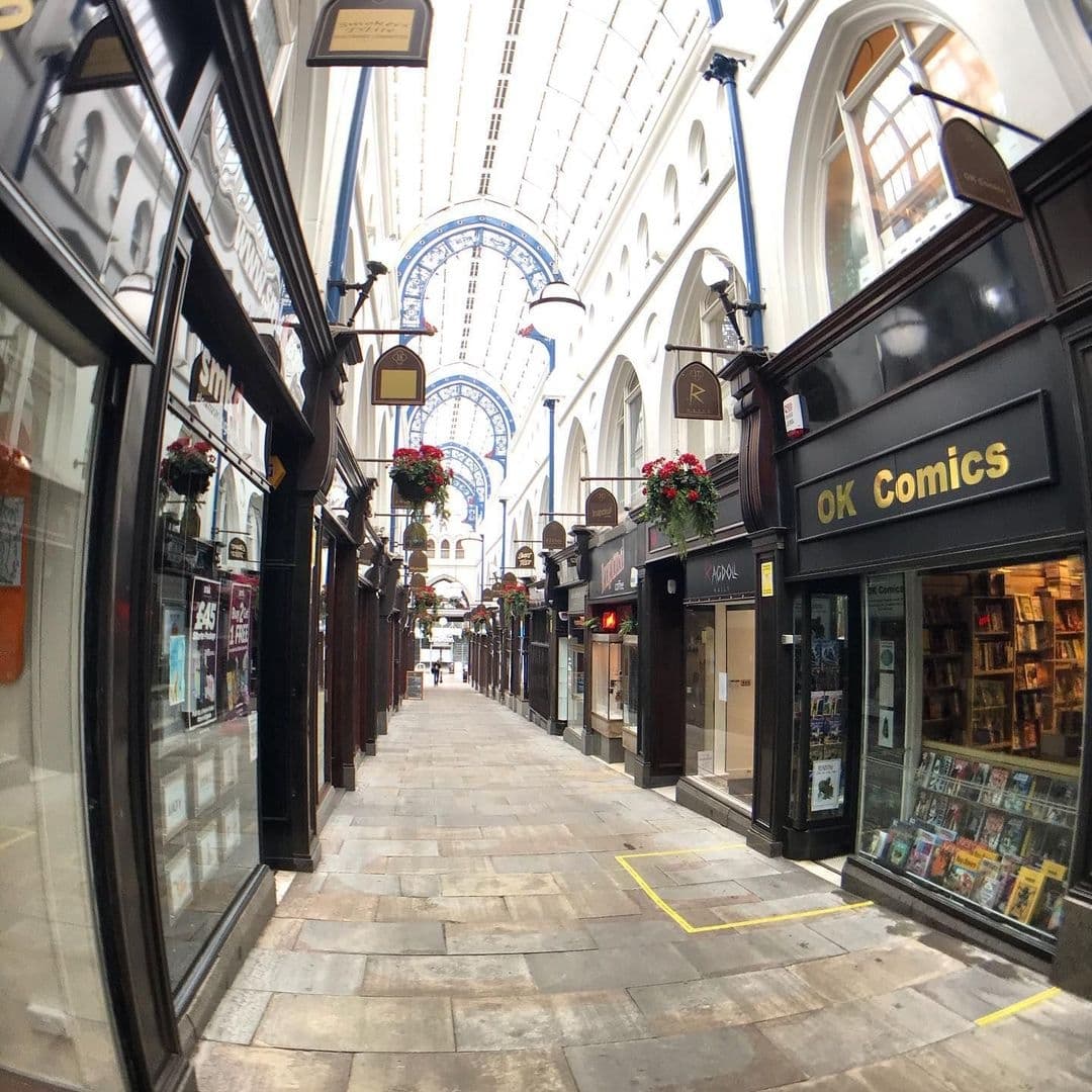 Kapow Coffee Thorntons Arcade Victorian Architecture Shopping Aisle Interior view of Thorntons Arcade with shops lining the sides, a glass roof overhead, and hanging flower baskets, leading towards Kapow Coffee.
