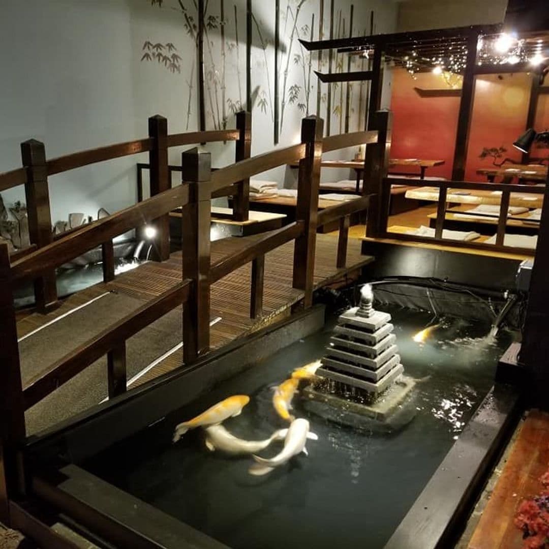 LittleTokyo IndoorKoiPond TranquilAmbiance DiningExperience Tranquil indoor koi pond with large fish and a tiered fountain at a dining venue in Little Tokyo.
