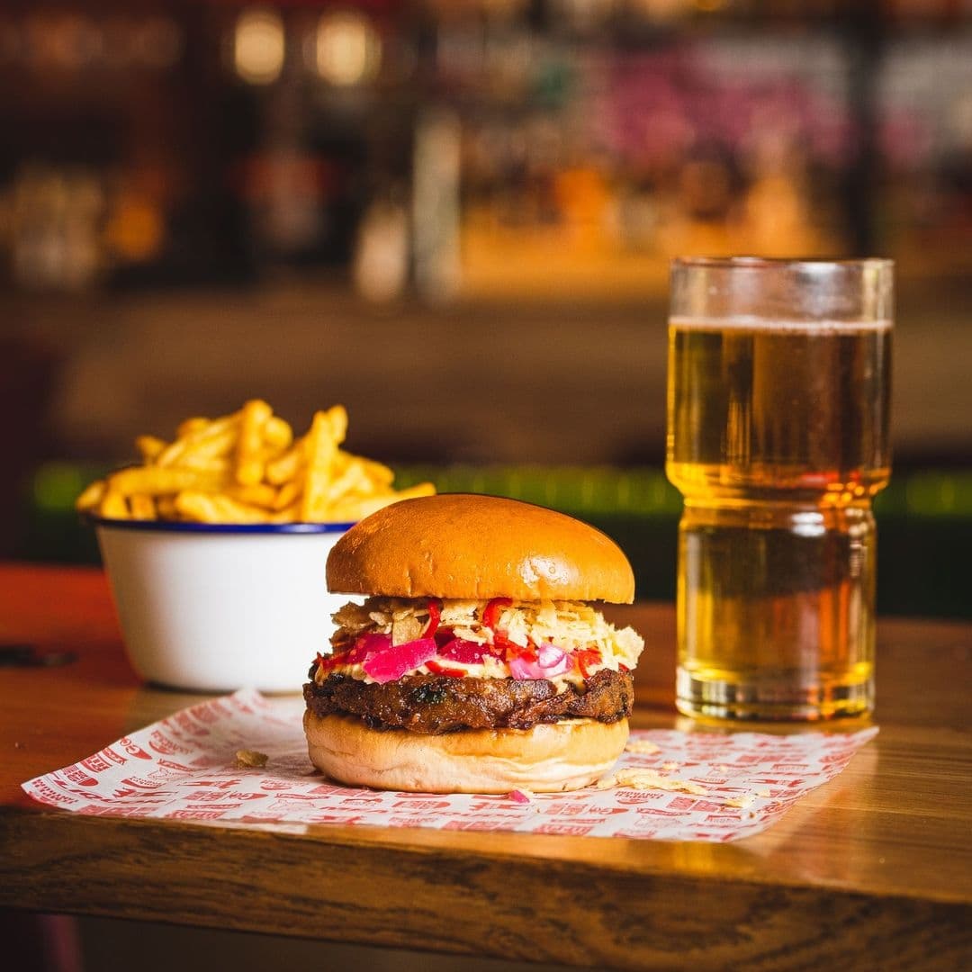 MEATliquor Burger Fries Beer PubAmbiance Juicy burger with toppings and fries on the side, accompanied by a glass of beer at MEATliquor.