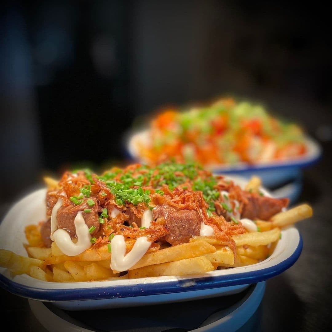 MadFransBar_GourmetLoadedFries_AppetizingMeal_Closeup Alt text: "Savory loaded fries topped with pulled pork, drizzled with creamy sauce, and sprinkled with fresh chives, served at Mad Frans Bar."