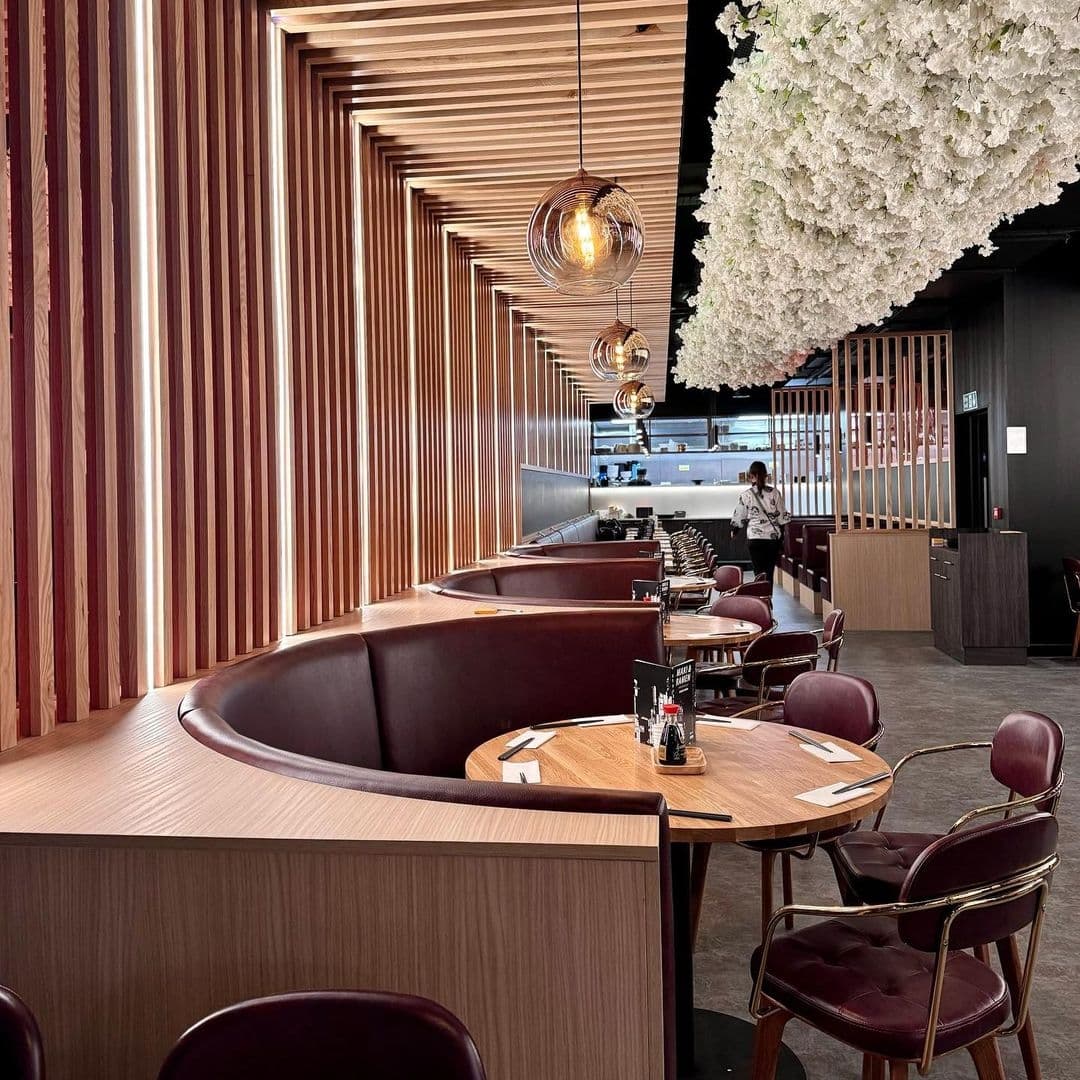 Maki Ramen Modern Interior Design Elegant Atmosphere Interior of Maki & Ramen featuring elegant wooden slat walls, modern spherical pendant lights, and plush curved seating with a large white floral installation overhead.