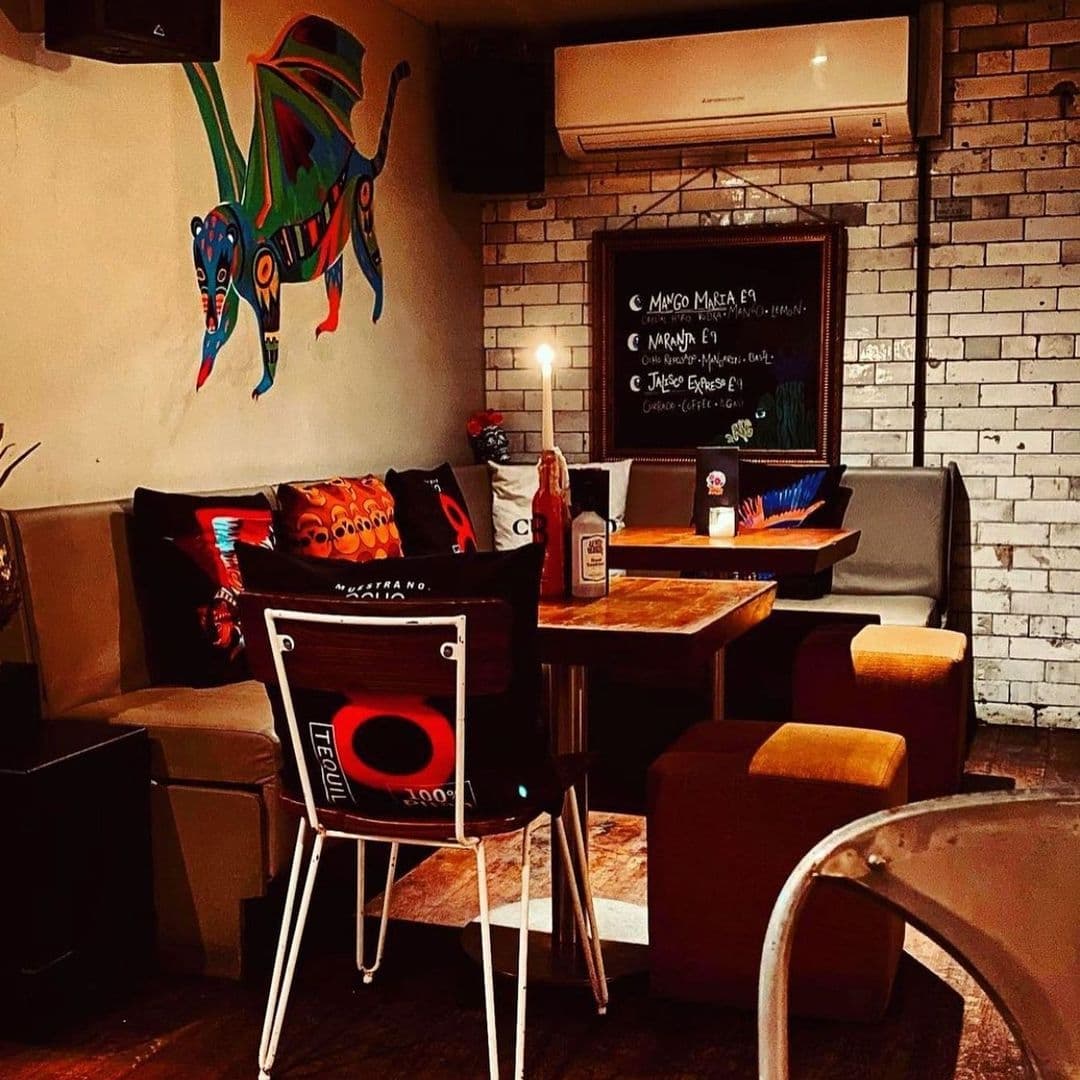 Neon Cactus Cozy Ambience Colorful Artwork Vintage Decor Cozy interior of Neon Cactus featuring eclectic decor with colorful wall art, cushioned seats, a chalkboard menu, and ambient lighting.