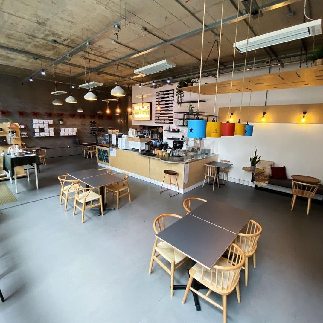 North_Star_Coffee_Shop_interior_modern_design_spacious Interior of North Star Coffee Shop with wooden tables and chairs, a counter with coffee machines, hanging lights, and colorful wall decorations.