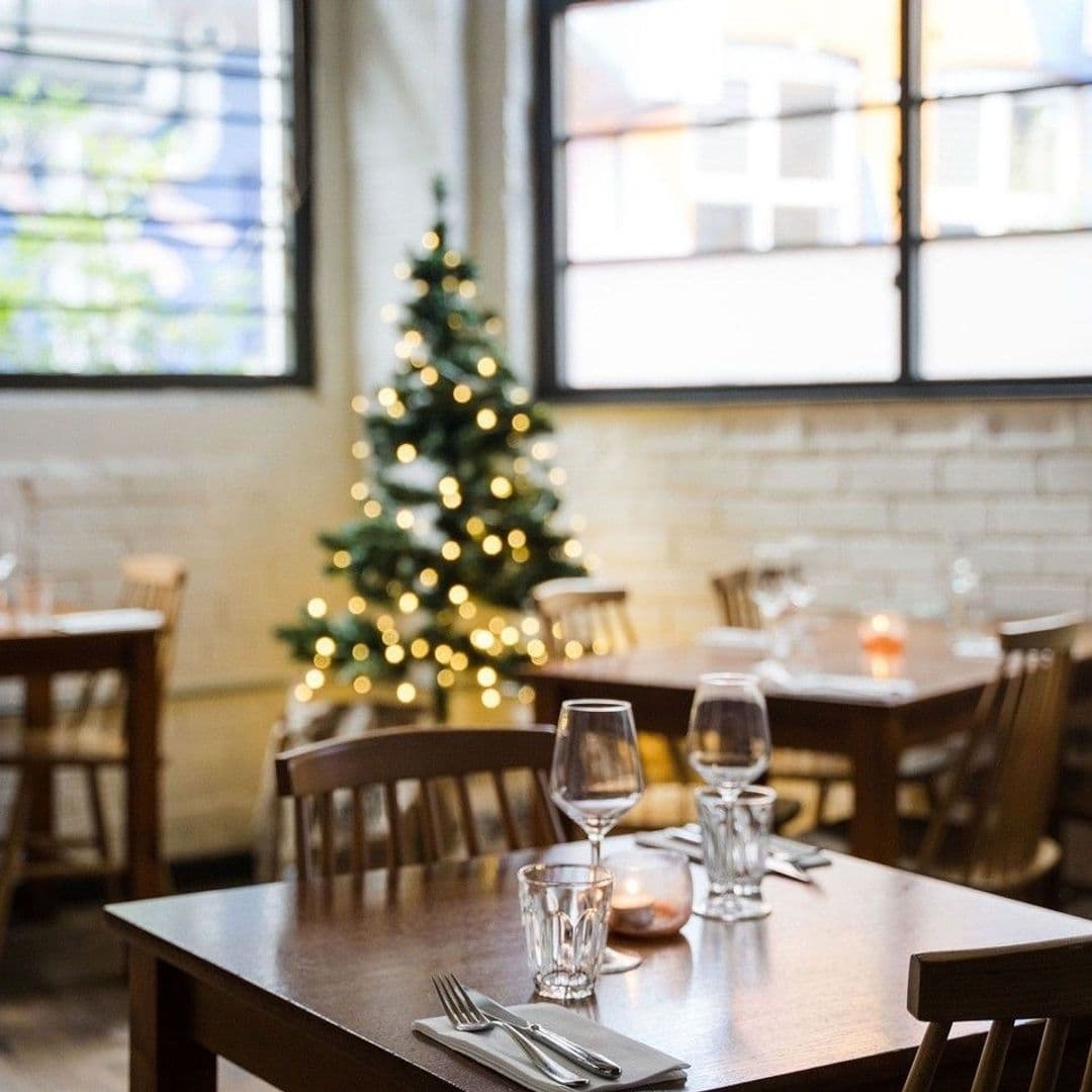 Ox Club at Headrow House Cozy Christmas Dining Setup Cozy dining setup at Ox Club at Headrow House with a decorated Christmas tree in the background, wooden tables set with glasses and cutlery, and warm lighting.