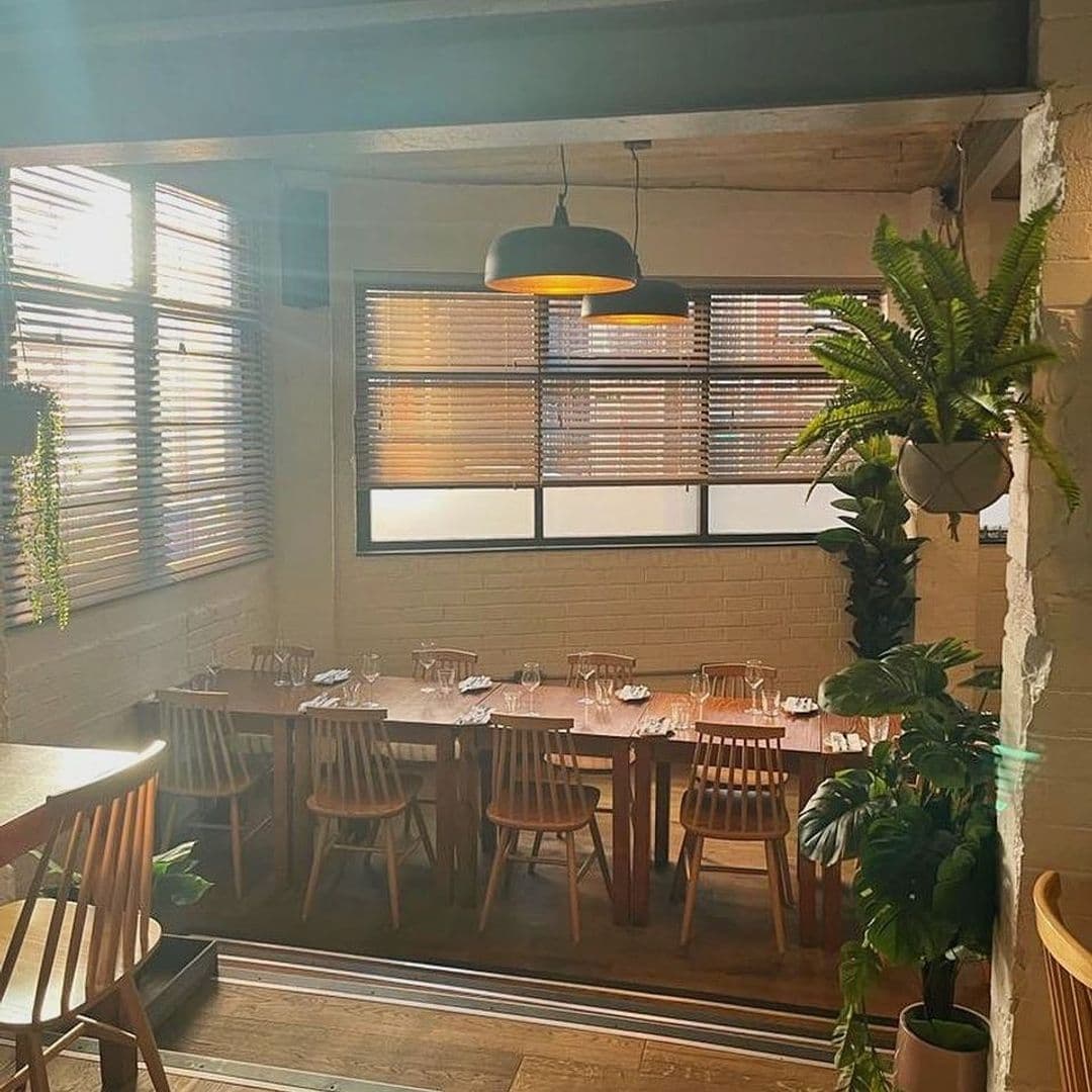 Ox Club at Headrow House Sunlit Dining Area Wooden Furniture Plants Interior of Ox Club at Headrow House featuring wooden tables set for dining, chairs, pendant lighting, and green potted plants with sunlight filtering through window blinds.