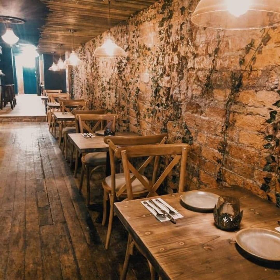 Phranakhon_RusticStoneWalls_WoodenFurniture_CozyAmbiance Rustic dining area in Phranakhon with wooden tables, exposed brick walls, and hanging pendant lights.