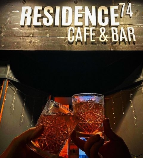 Residence Bar Cafe Kitchen Headingley Cheers Evening Drinks Two hands toasting with pink drinks in patterned glasses at Residence Bar Cafe | Kitchen (Headingley), with the illuminated sign of the establishment in the background.
