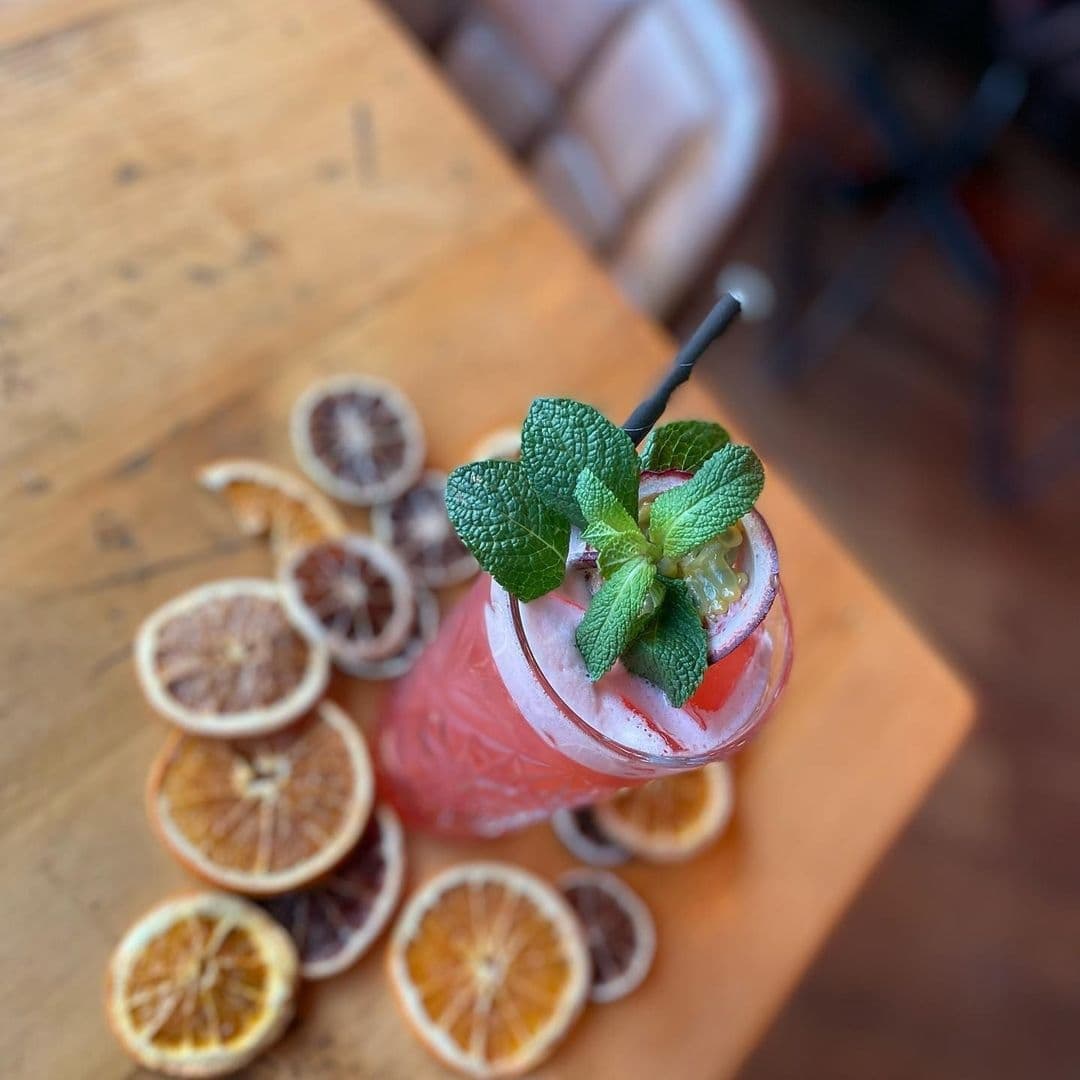 Residence Bar Cafe Kitchen Headingley_Signature Cocktail Fresh Mint Citrus Decor Refreshing cocktail garnished with mint on a wooden table at Residence Bar Cafe | Kitchen (Headingley), surrounded by dried citrus slices.