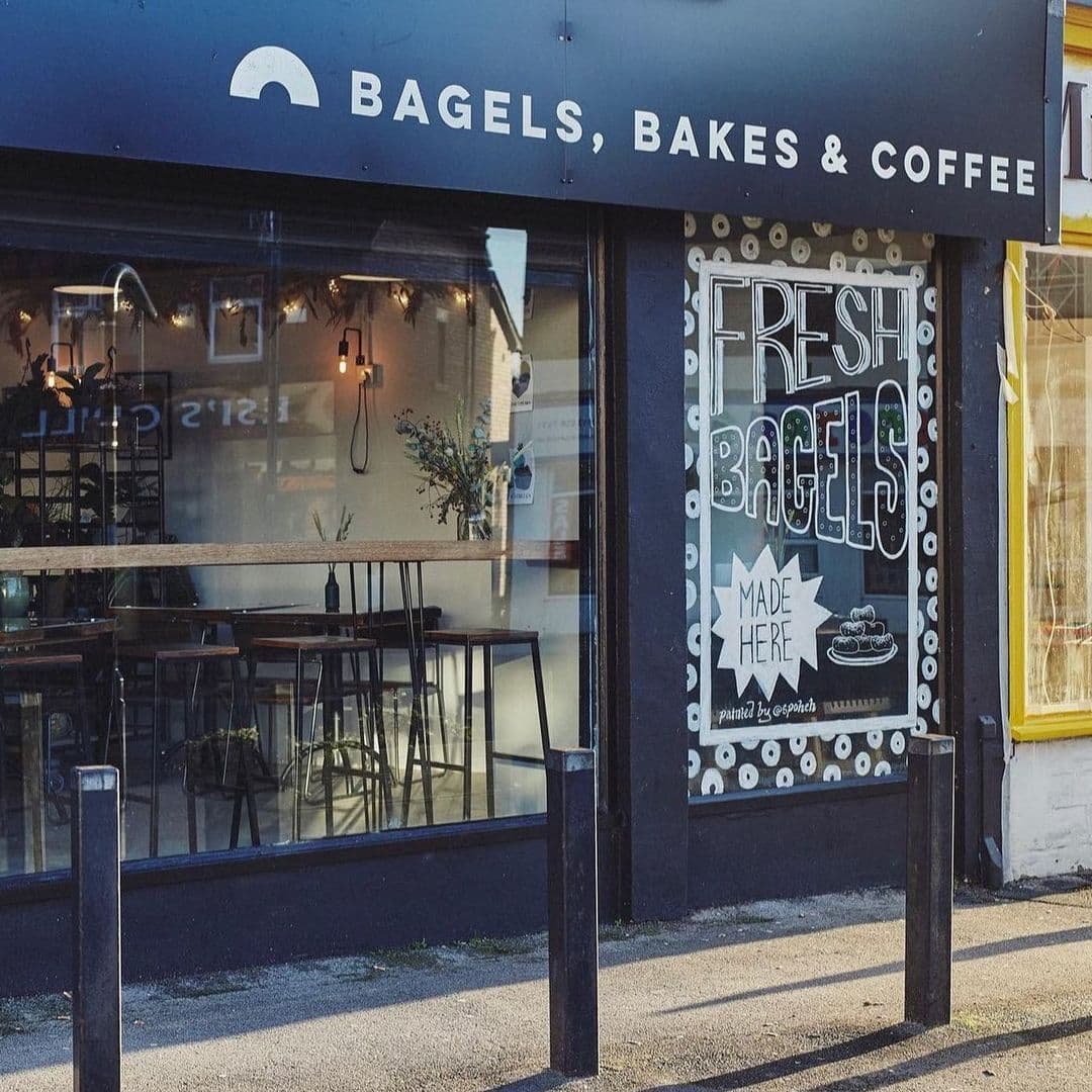 Slow Rise Bakery Exterior Bagels Signage Cafe Window Exterior view of Slow Rise Bakery featuring a sign that reads "Bagels, Bakes & Coffee" above large window with "Fresh Bagels Made Here" artwork, cozy interior with tables visible.