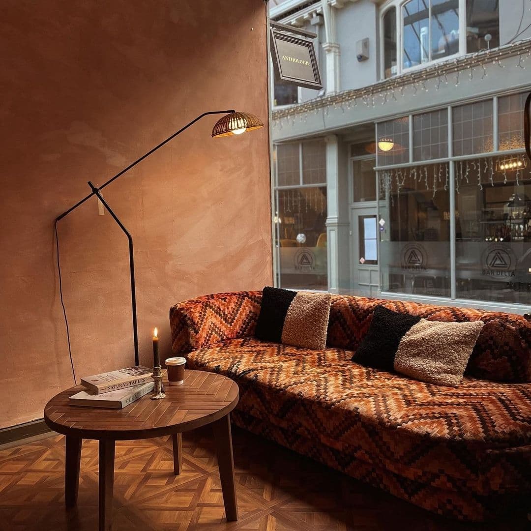 Sonder_CozyCornerPatternedCouchWarmLighting Cozy corner at Sonder with a patterned sofa, wooden round table, floor lamp, and a view of the street through the window.