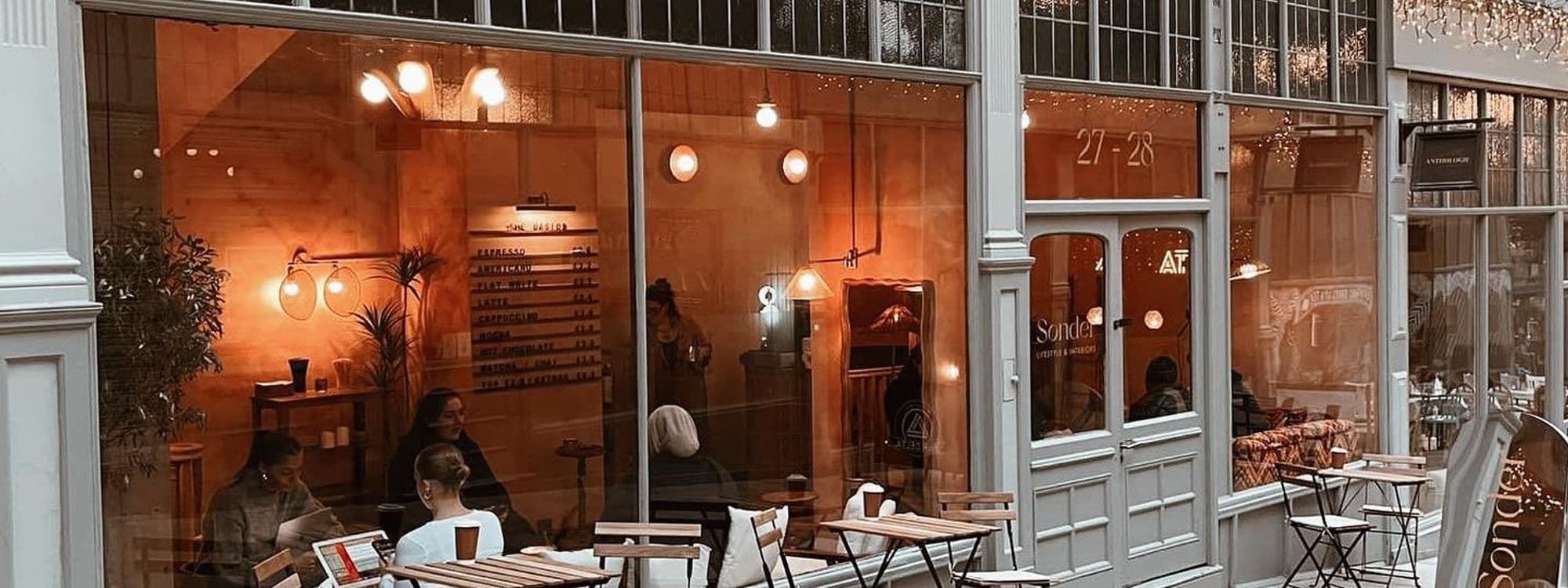 Exterior view of Sonder coffee shop with warm lighting, patrons seated inside and outside, and a visible menu board through the window.