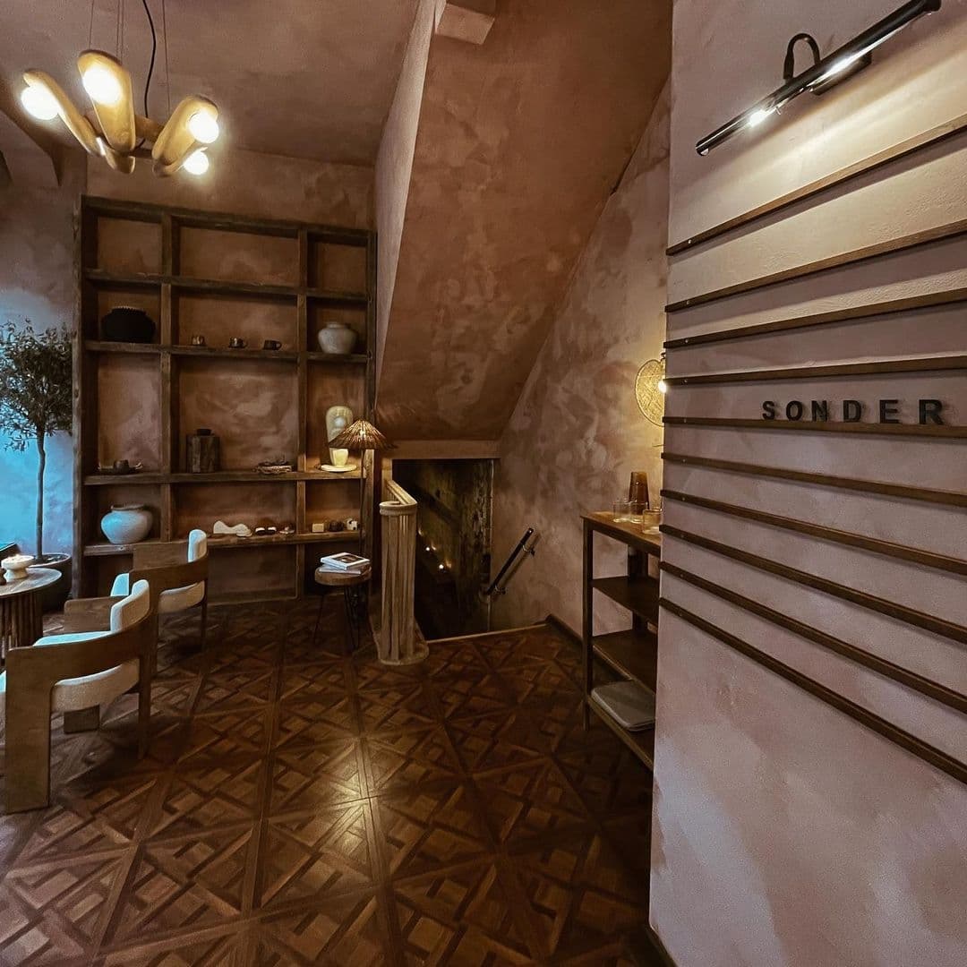 Sonder_RusticChicInterior_DesignElements_WarmLighting Interior of Sonder featuring rustic decor with textured walls, wooden furniture, patterned floor tiles, and warm lighting. The name 'SONDER' is displayed on a wall.