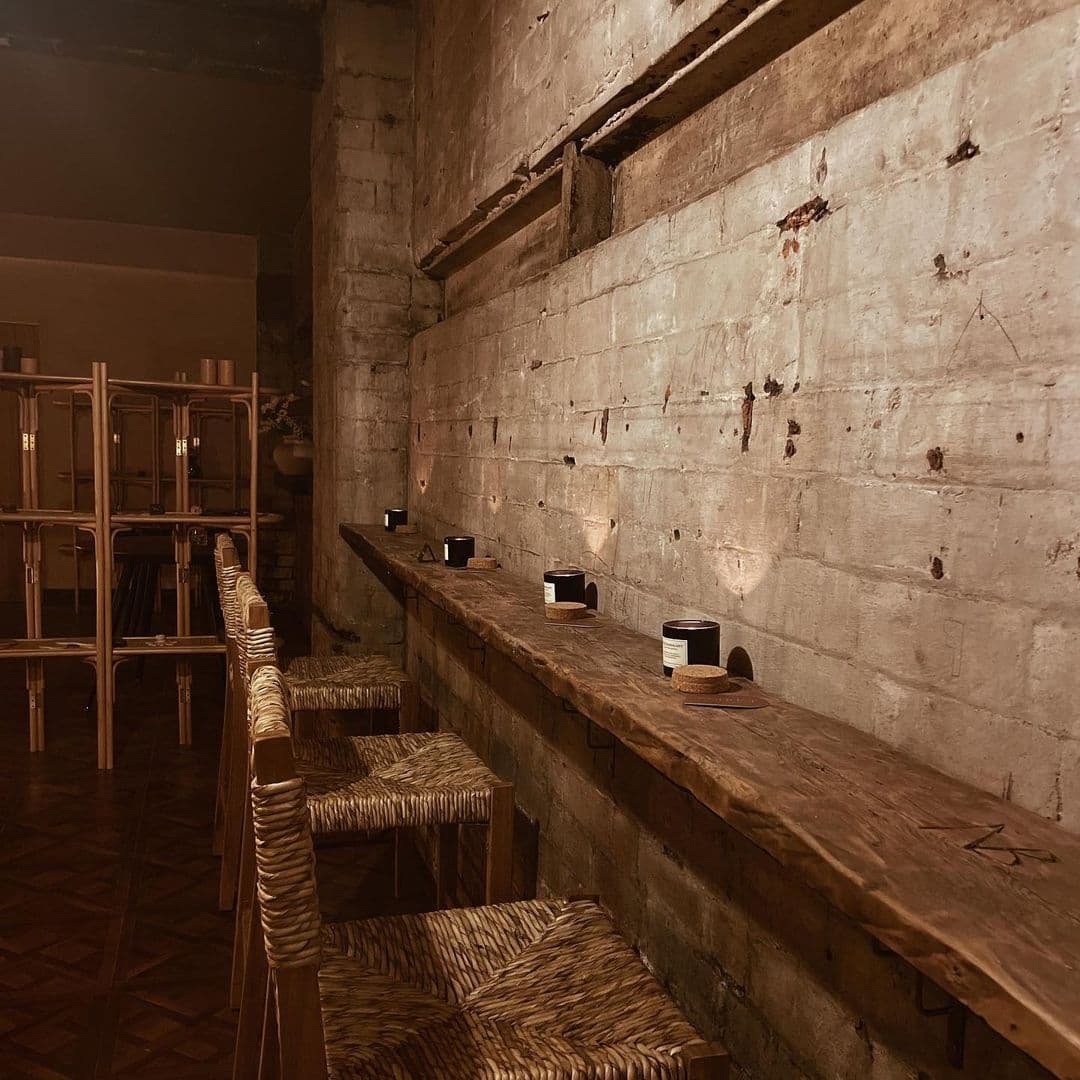 Sonder_Rustic_Bar_Interior_Wooden_Details Rustic interior of Sonder featuring a wooden bar counter with stools against a textured concrete wall, dimly lit for an intimate atmosphere.