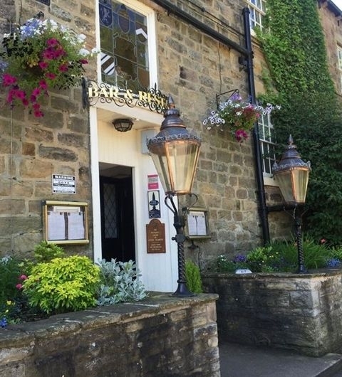 The Bingley Arms Historic Pub Entrance Lanterns Flowers Entrance of The Bingley Arms with lit lanterns, hanging flower baskets, and a stone facade.