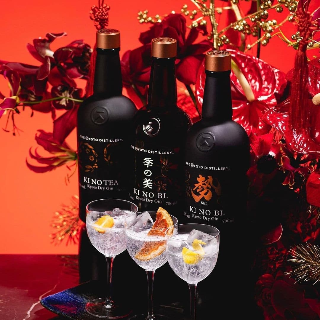 The Ivy Asia_Kyoto Gin Bottles Cocktails Elegant Decor Elegant display at The Ivy Asia featuring three bottles of KI NO BI Kyoto Dry Gin with garnished gin and tonics in the foreground, set against a vibrant orange backdrop with decorative red flowers.