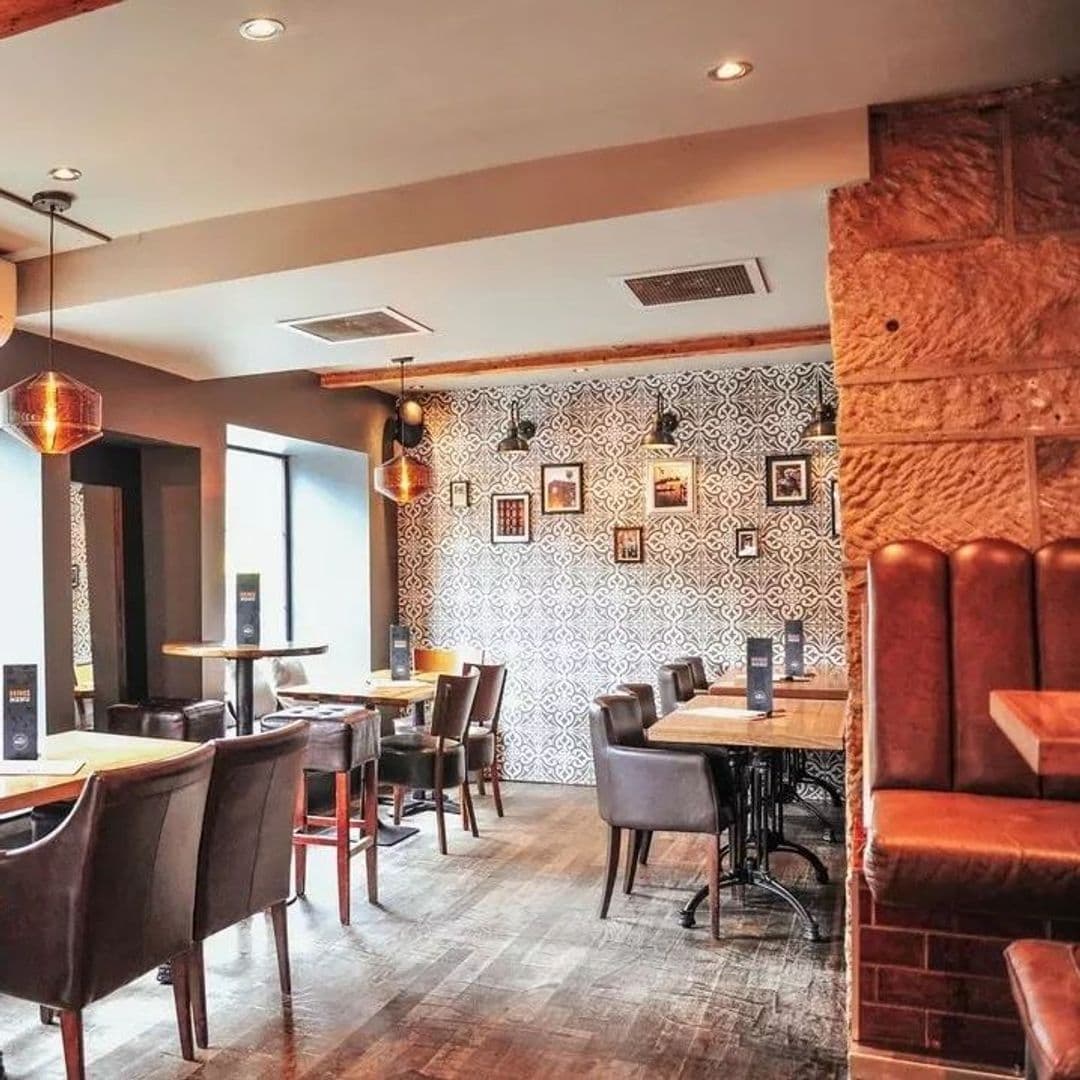 The Malt Brewhouse Cozy Interior Design Warm Lighting Interior of The Malt Brewhouse featuring a cozy seating area with leather chairs, wooden tables, decorative wallpaper, and pendant lighting.